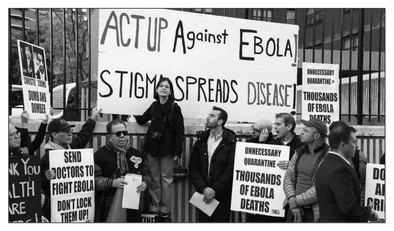 Photo of people with signs demonstrating, with caption: From TAG Update December, 2014: TAG's Jeremiah Johnson joined ACT UP and allies outside Bellevue Hospital in New York City to demand evidence-based policies that support health care workers fighting Ebola. (Future TAG staff member Annette Guadino is standing in middle)
