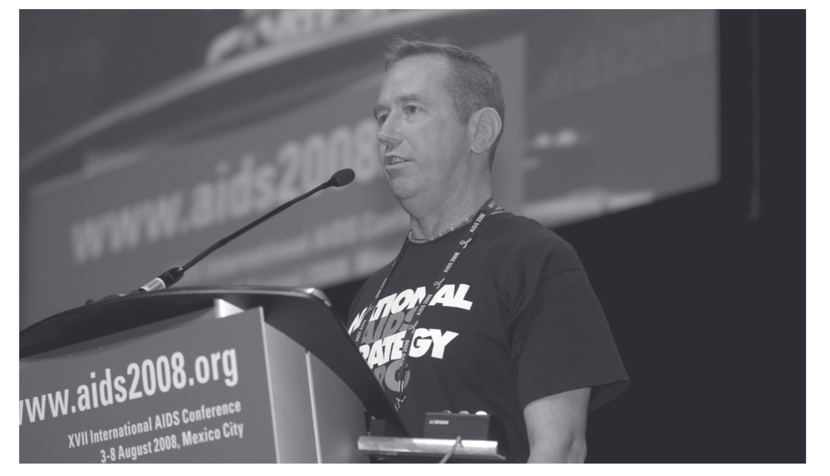 Mark Harrington at podium with caption: TAG executive director Mark Harrington addressed the XVII International AIDS Conference 2008 in Centro Banamex, Mexico City, August 8, 2008.