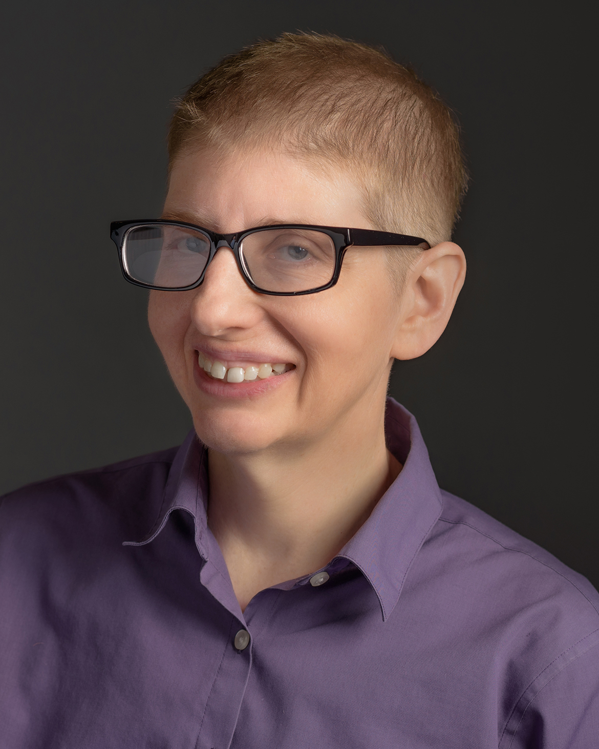 headshot of Laura Morrision, TAG Board member, Treasurer, and 2022 RIAA Honoree. White woman with glasses and short hair, wearing a purple collared shirt