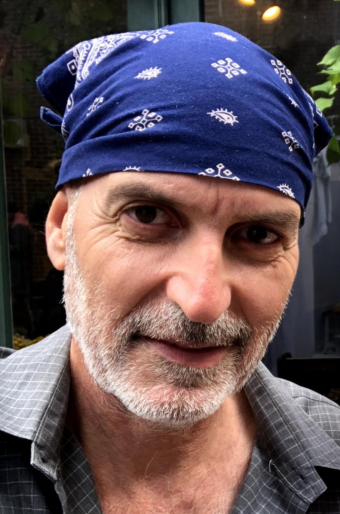 older man with slight beard, looking directly at camera and wearing a bandana on his head