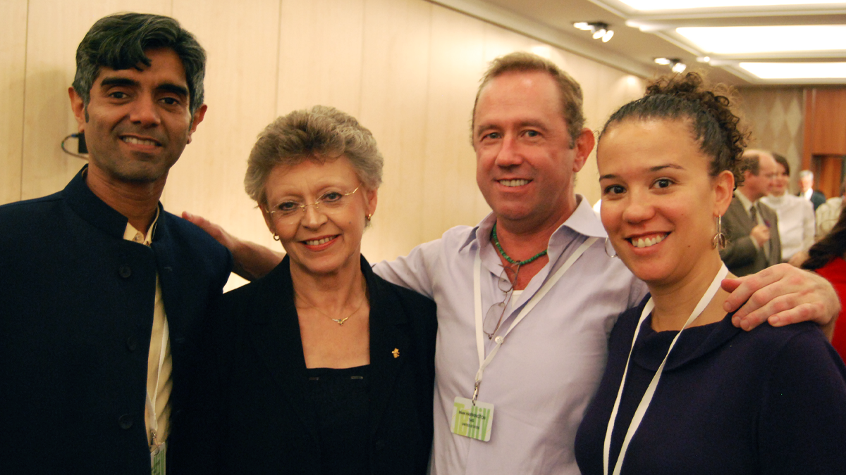 Four people looking at the camera in the hallway during a conference; one of them has his arm around two
