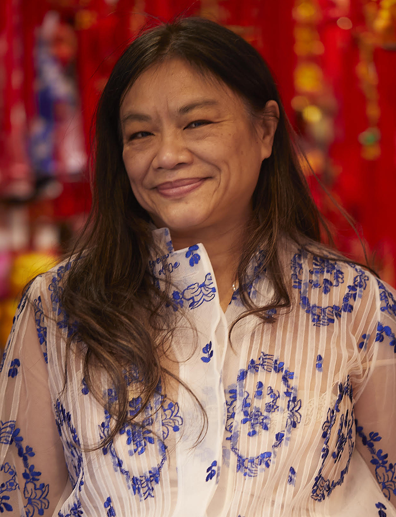 Asian woman smiling and looking at the camera. wearing a gauzy blue and white shirt/dress