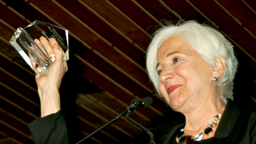 Older White Woman With White Hair Holding Up A Glass Award
