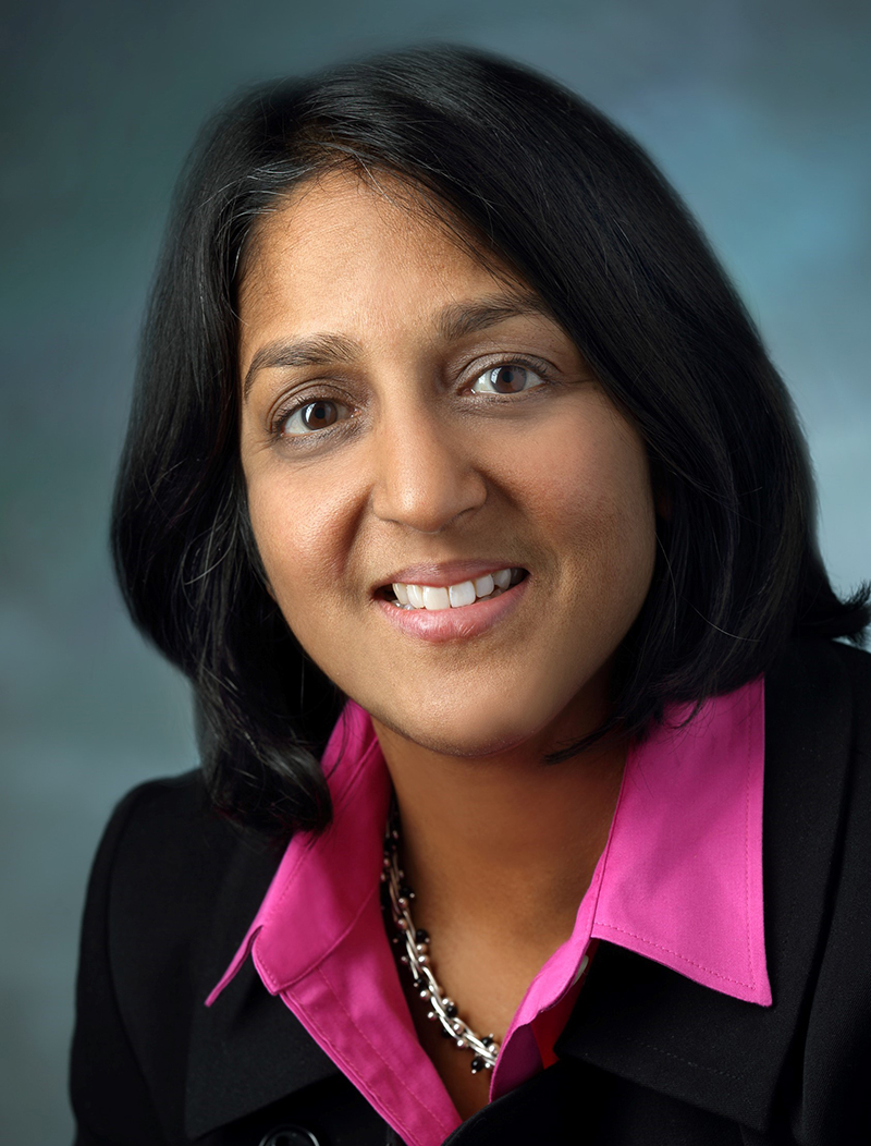 woman with medium tan skin and black hair looking at camera; wearing a pink collared shirt and black jacket