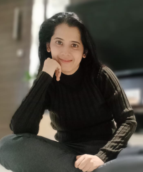 Photo of Keyuri Bhanushali: Indian woman sitting with her legs crossed, smiling, wearing a dark green sweater and grey pants