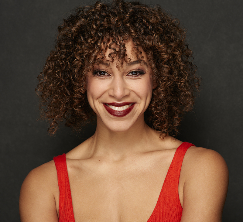 Photo of RIAA 2023 emcee, Tamrin Goldberg. Black woman smiling, with curly hair and wearing a sleeveless red dress