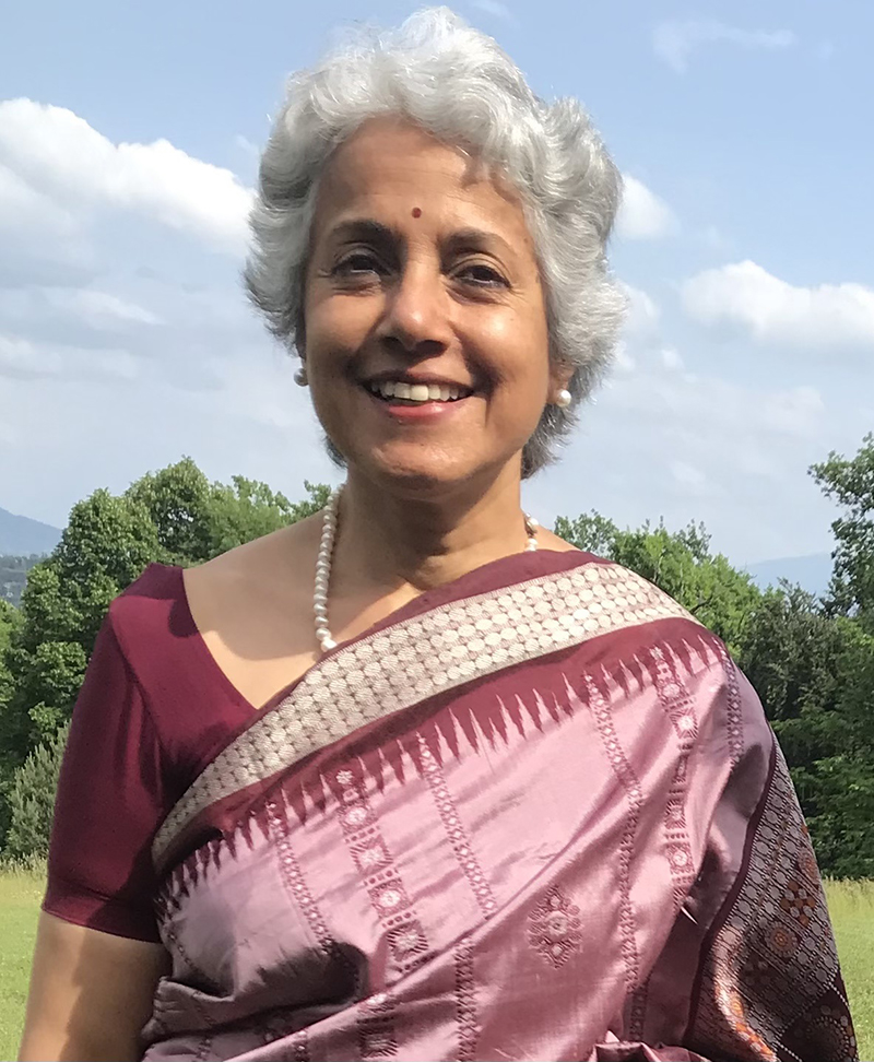 Photo of a smiling Indian woman with grey hair, wearing a pearl necklace and tones-of-pink sari