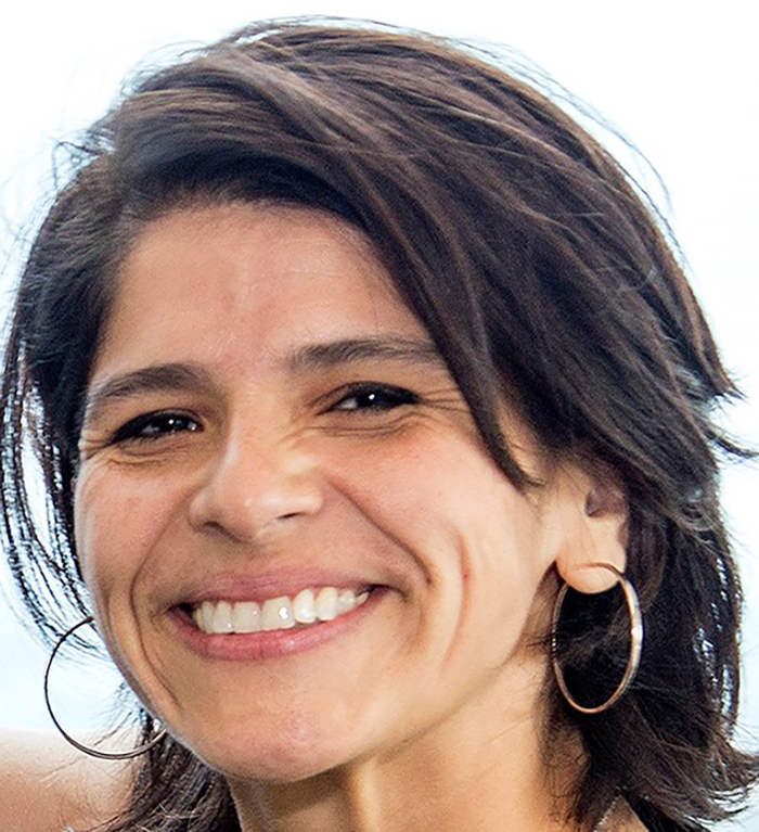 Woman with dark hair who's smiling and wearing silver hoop earrings