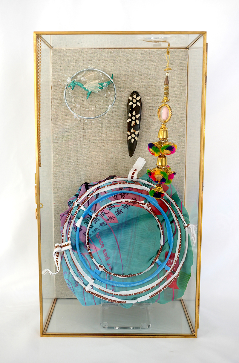 A photo of one of the unique 2023 Limited Art Editions by Ivy Kwan Arce. A variety of colorful elements enclosed in a glass vitrine