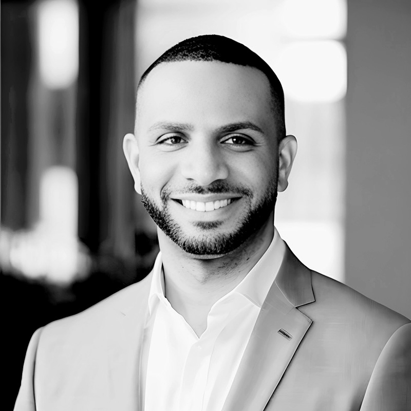 photo of black man, smiling, wearing an open white shirt and jacket